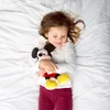 A young girl is lying on a white bed with a Mickey Mouse plush toy. Voir les images du produit