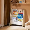 A children's bookshelf filled with books, placed in a room with curtains and a rug. Produktbild-Vorschau