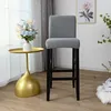A bar stool with a grey cover is placed next to a gold side table with a vase of flowers. Produktbild-Vorschau