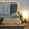 A cozy living room scene with a couch, coffee table, and a lamp, decorated with string lights. Produktbild-Vorschau