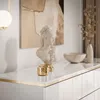 A white dresser with gold trim, decorated with a bust, a bowl, and a vase with dried flowers. Produktbild-Vorschau
