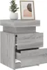 A close-up view of a gray wooden nightstand with two drawers, one partially open, and a framed picture and a potted plant on top. Podgląd zdjęcia produktu