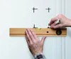 A person is using a spirit level and a marker to draw lines on a wall. Podgląd zdjęcia produktu