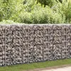 A gabion wall made of stones in a wire cage, set against a backdrop of green foliage and grass. Náhled obrázku produktu