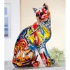 A colorful, graffiti-style cat figurine sits on a white surface with a blurred background. Produktbild-Vorschau