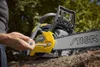 A person is adjusting a chainsaw that is resting on a log, with trees in the background. Produktbild-Vorschau