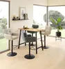 A modern dining area with a bar table and stools, set against large windows with a view of greenery. Produktbild-Vorschau