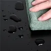 A hand wiping water droplets off a black surface with a green cloth. Produktbild-Vorschau