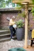 A woman watering a plant in a large pot on a patio. Voir les images du produit