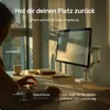 A person is working at a desk with a monitor mounted on a stand. Sunlight streams in from a window. Produktbild-Vorschau