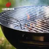 A close-up shot of a black charcoal grill with flames and smoke rising from the coals. Produktbild-Vorschau