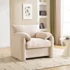 A beige armchair is placed in a living room setting, with shelves and curtains in the background. Produktbild-Vorschau