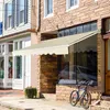 A cream-colored awning extends over a storefront window, with a bicycle parked on the sidewalk in front. Anteprima dell’immagine prodotto