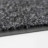 Close-up view of the edge of a dark gray carpet mat with a black rubber backing. Voir les images du produit