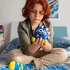 A child sitting on a bed holding a blue monster toy. Voir les images du produit