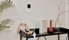 A baby monitor camera is mounted on a flexible arm above a shelf with a stuffed bunny, books, and vases. Náhled obrázku produktu