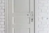 A close-up view of a white door with a silver handle and a white brick wall next to it. Anteprima dell’immagine prodotto