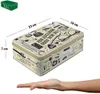 A tin box with various illustrations and dimensions indicated, placed on a white background with a hand underneath for scale. Voir les images du produit
