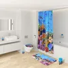 A brightly lit bathroom with a shower curtain, toilet seat, and bath mat featuring an ocean theme with fish and coral. Produktbild-Vorschau