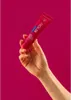 A hand holds a tube of toothpaste against a vibrant pink background. Náhled obrázku produktu