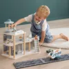 A young boy plays with a wooden airport toy set on the floor. Voir les images du produit