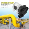 A small water pump is shown in the foreground, with large yellow industrial pipes in the background. Voir les images du produit