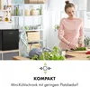 A woman is preparing food in a kitchen, with a mini-fridge visible on a shelf. Produktbild-Vorschau