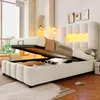 A bedroom scene with a bed that has its storage compartment open, revealing items inside. The bed has a padded headboard with LED lighting. Produktbild-Vorschau
