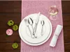 A table setting with cutlery, plates, a wine glass, and floral decorations on a pink runner. Náhled obrázku produktu