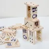 A collection of wooden dominoes, some stacked to form a structure, others scattered on a white surface. Produktbild-Vorschau