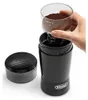 A hand is holding a clear container filled with coffee grounds over a black coffee grinder. Podgląd zdjęcia produktu