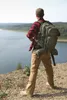 A person wearing hiking gear stands on a rocky outcrop overlooking a body of water and a forested landscape. Anteprima dell’immagine prodotto