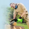 An older man with long gray hair and glasses is using a small electric chainsaw to cut a log in an outdoor setting. Produktbild-Vorschau
