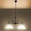 A black wrought iron chandelier with two white glass shades hangs from a chain against a gradient brown background. Produktbild-Vorschau