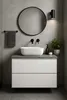 A modern bathroom vanity with a white sink, gray countertop, and white drawers, set against a tiled wall. Produktbild-Vorschau