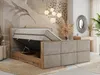 A bedroom scene featuring a large, open bed with storage compartments. The bed has a padded headboard and frame in a beige textured fabric, with wooden accents. The room is decorated with a nature-inspired mural, decorative plants, and a modern chandelier. Produktbild-Vorschau