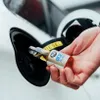 A hand is pouring a liquid from a small bottle into a car's fuel tank opening. Produktbild-Vorschau