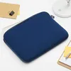 A blue laptop sleeve is shown on a white surface with a notebook and binder clip to the left, and a notepad and pen to the right. Produktbild-Vorschau