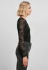 A woman is shown from the side wearing a black lace long-sleeved bodysuit and dark jeans against a plain gray background. Produktbild-Vorschau