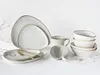 A collection of ceramic tableware, including plates, bowls, and mugs, arranged on a white surface with decorative dried branches. Náhľad obrázku produktu