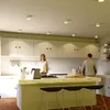 A modern kitchen scene with two people, a woman standing behind a kitchen island and a man standing near the counter. Produktbild-Vorschau