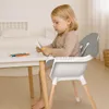 A young child is sitting at a table in a high chair, cutting paper with scissors. Voir les images du produit