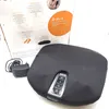A black foot massager with a control panel and its power adapter are shown on a white and light gray background. Part of the product's packaging is visible in the background. Produktbild-Vorschau