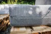 A close-up of a gray, corduroy-textured cushion or mattress with a zipper, resting on wooden pallets outdoors. Produktbild-Vorschau