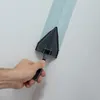 A hand is holding a paint roller with a blue paint stripe on a white wall. Voir les images du produit