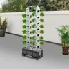 A vertical hydroponic garden tower with plants growing on a balcony or patio, with a potted plant and a wall in the background. Podgląd zdjęcia produktu