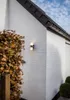 An outdoor LED wall light is mounted on the corner of a white brick building. Anteprima dell’immagine prodotto