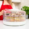A person is holding a food dehydrator filled with mushrooms and vegetables. Náhľad obrázku produktu