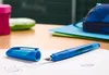 A blue fountain pen and its cap are placed on a notebook on a desk, with school supplies in the background. Náhľad obrázku produktu