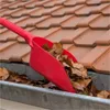 A red gutter scoop is being used to clean fallen leaves from a gutter, with a tiled roof in the background. Produktbild-Vorschau